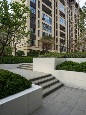 Temiz, modern bir beyaz taş merdiven canlı yeşillikler arasında yerleşim parkı ortamında kıvranıyor. Görüntü yapısal zarafeti, meditasyon hareketini ve barışçıl manzara tasarımını aktarıyor. Yüksek kalitede gerçek fotoğrafçılık ve sığ fi derinliği