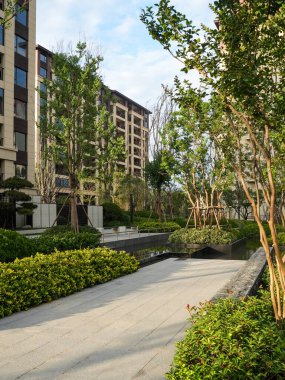 Yeşil, iyi tasarlanmış, yüksek ağaçlı bir bahçe parkının içinden geçen sakin, asfalt bir yol. Görüntü sessiz bir geri çekilme, doğal güzellik, mimari denge ve temiz hava sağlıyor. Sığ derinlikli yüksek kaliteli gerçek fotoğrafçılık