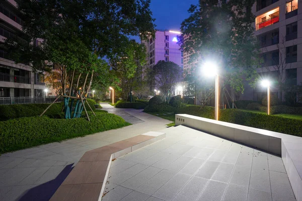 Parlayan direklerle aydınlatılan, geceleri ağaçlar ve çalılarla aydınlatılan bir yerleşim parkında huzurlu bir yol. Görüntü, akşam sükunetini, toplum yaşamını, mimariyi ve sükuneti aktarıyor. Yüksek kalitede gerçek fotoğrafçılık ve sığ fi derinliği