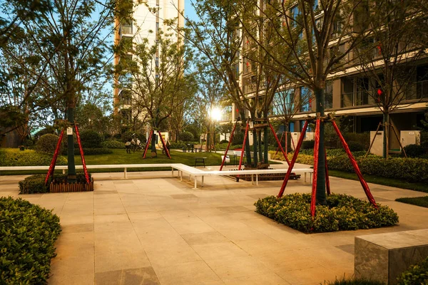 Sıcak altın saat ışığında parlayan, taştan koltukları ve güneş lekeli ağaçlarıyla huzurlu bir bahçe alanı. Görüntü sıcaklığı, doğal güzelliği, dinginliği ve dışarıdaki konforu yansıtıyor. Sığ alan derinliğine sahip yüksek kaliteli gerçek fotoğrafçılık.