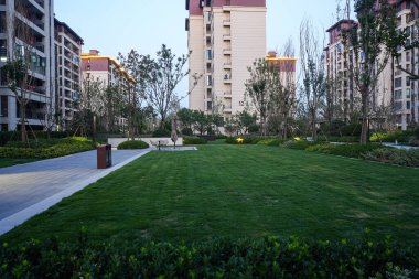 Akşam geçişi sırasında canlı yeşil çimlerin ve modern apartmanların bulunduğu sakin, manzaralı bir yerleşim yeri. Görüntü toplum huzurunu, refahını, doğa entegrasyonunu ve üst düzey kentsel yaşam tarzını aktarıyor. Yüksek kalite gerçek