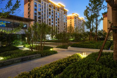 Modern demirbaşlarla aydınlatılan ve geceleri yemyeşil yeşilliklerle çevrili konut parkında parlayan bir patika. Görüntü güvenliği, akşam sükunetini, mimariyi ve huzur içinde yaşamayı sağlar. Sığ alan derinliğine sahip yüksek kaliteli gerçek fotoğrafçılık