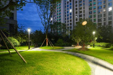 Huzurlu bir konut parkında gece yakalanan güzel, aydınlık, dolambaçlı bir bahçe yolu. Görüntü, rahatlamayı, akşam güzelliğini, toplum güvenliğini ve uyumlu manzara tasarımını iletir. Sığ alan derinliğine sahip yüksek kaliteli gerçek fotoğrafçılık.