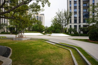 Yeşil katmanlı çimleri, taş yolları ve olgun ağaçları olan güzel manzaralı bir bahçe alanı. Resim tasarım düzenini, doğa bağlantısını, huzurlu toplum yaşamını ve refahı iletir. Sığ derinliğe sahip yüksek kaliteli gerçek fotoğrafçılık
