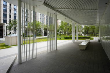 Beyaz dikey kolonların yer aldığı, temiz çizgili, modern bir bahçe pavyonu, parkta huzurlu, korunaklı bir alan sunuyor. Görüntü tasarım ritmi, açık hava sakinliği, toplum uyumu ve modern mimari güzelliği taşır. Yüksek kaliteli gerçek fotoğrafçılık.