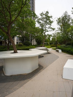 Sessiz bir bahçe parkında, olgun bir ağacın etrafına yapılmış eşsiz, beyaz, heykel tezgahı. Görüntü, doğa bağlantısını, tasarım yeniliklerini, toplum huzurunu ve açık hava rahatlığını aktarıyor. Sığ alan derinliğine sahip yüksek kaliteli gerçek fotoğrafçılık.