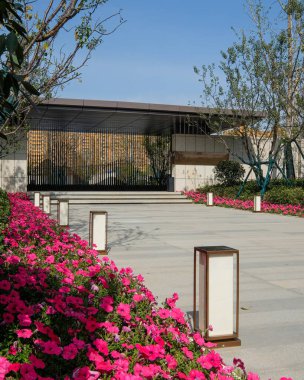 Tarif: Modern bir bina girişine giden pembe çiçeklerle çevrili bir patika. Hoş bir atmosfer, peyzaj güzelliği ve profesyonel erişim sağlıyor. Yüksek kaliteli gerçek fotoğrafçılık..