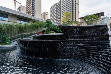 Şelale manzarası, bahçe ağaçları, modern şehir binası.