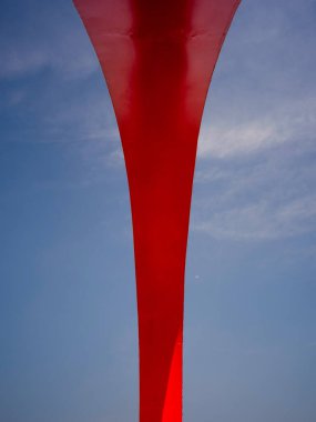 Büyük kırmızı bir heykelin tabanına ve destek sütununa yakından bakmak. Görüntü endüstriyel mimariyi, kalın tasarımı ve biçimi aktarıyor. Yüksek kalite fotoğrafçılık.