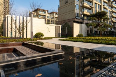 Tarif: Bahçedeki katmanlı su özelliği, modern bina ve gökyüzünü yansıtıyor. Görüntü, Zen manzarası, sükunet ve barışçıl atmosfer taşır. Yüksek kalite fotoğrafçılık.