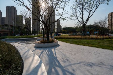 Tarif: Olgun ağaçlar ve modern yerleşim yeri olan manzaralı bir park manzarası. Görüntü, şehir doğası, mimarisi ve tasarımı taşır. Yüksek kalite fotoğrafçılık.