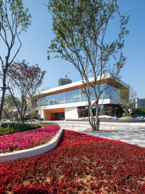 Renkli çiçeklerle dolu canlı bir bahçeye bakan büyük cam pencereli modern bir bina. Görüntü kentsel dinginliği, doğayı ve mimariyi aktarır. Yüksek kalite fotoğrafçılık.