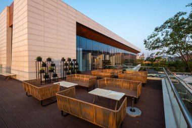 Modern bir binanın yanında, gün batımının sıcacık ışığıyla yıkanmış davetkar bir bahçe salonu. Görüntü, mimari rahatlama ve açık havada yaşam sağlıyor. Yüksek kalite fotoğrafçılık.