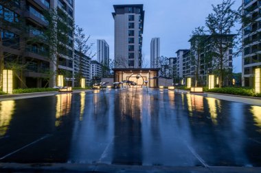 Açıklama: Bir su plazasının sakin bir akşam manzarası konut binalarını ve ışıkları yansıtıyor. Görüntü, manzara sükuneti, tasarım ve mimariyi taşır. Yüksek kalite fotoğrafçılık.