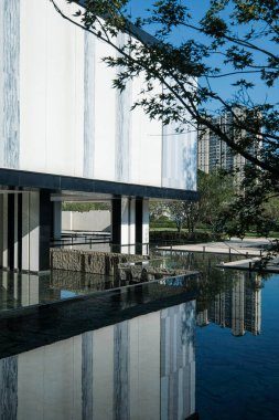 Açıklama: uzun, beyaz bir mimari bina cephesi çevreleyen bahçe ağaçlarıyla dolu bir havuza yansıdı. Görüntü mimariyi, tasarımı ve doğayı taşır. Yüksek kalite fotoğrafçılık.
