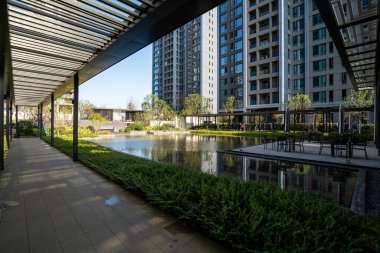 Açıklama: Parktaki sakin bir su birikintisinin yanındaki geçitte gölgeler bırakan mimari bir pergola. Görüntü tasarım, sükunet ve doğa taşır. Yüksek kalite fotoğrafçılık.