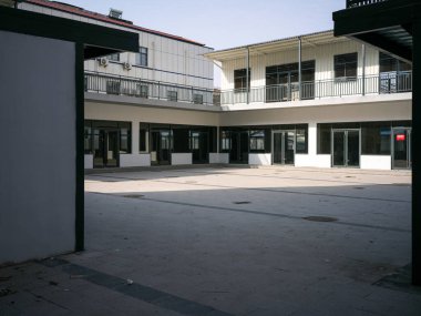 Temiz, boş asfalt bir avlu geniş bir görüş. Tamamen beyaz çok katlı binalarla çevrili. Parlak bir gökyüzünün altında siyah pencere çerçeveleri var. Kurumsal ortamları, kampüs yaşamını, yapısal düzeni ve kentsel durgunluğu taşır.