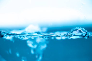 Hava kabarcıkları ve dalgalanmalarla mavi su yüzeyi, temiz sıvı arka plan, tazelik ve saflık kavramı, parlak ışık altında makro su hattı.