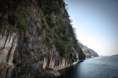 Sakin dağ gölü boyunca uzanan dramatik kaya uçurumu berrak gökyüzü altında, desenli taş duvarlı manzaralı vahşi doğa manzarası ve kopyalama alanı..