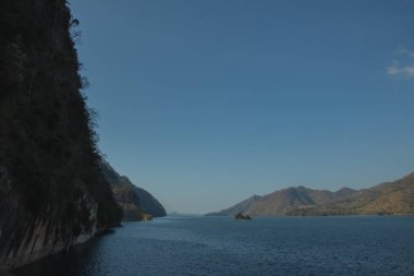 Berrak mavi gökyüzünün altında geniş bir dağ gölü, küçük bir ada ve sakin bir su, fotokopi alanı olan huzurlu doğa manzarası..
