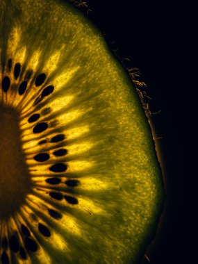 Kesilmiş kivi meyvesinin gözle görülür tohumları ve şeffaf dokusu olan makro yakın çekimi koyu bir arka planda..