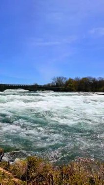 Güneşli bir günde, arkaplanda açık mavi gökyüzü ve akan suyla Niagara Şelalesini ziyaret edin..