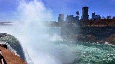 Ontario, Kanada, 9 Ağustos 2025: Niyagara Şelalesi 'ni açık gökyüzü, akan su ve gün içinde yakınlardaki bina ve yapıların görüntüleriyle ziyaret edin. İnsanlar parlak gökyüzünün altında Niagara Şelalelerini keşfediyorlar..