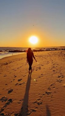 Gün batımında kumsalda yürüyen kadın. Gün batımında okyanus sahilinde yürüyen bir kadın silueti..