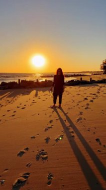 Akşamları okyanus kenarında yürüyüş. Gün batımında huzurlu sahil yürüyüşünün tadını çıkaran kişi.