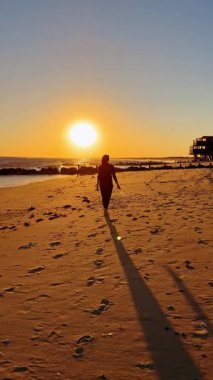 Kumsal gün batımına doğru yürü. Güneşin batışına doğru kumlu sahilde yürüyen biri..