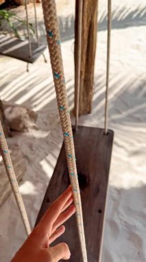 Güneş ışığı altındaki kumlu bölgede ahşap destekli ve ipli salıncaklar. Güneş ışığı altında, kumlu bir alanda, ahşap bir yapıda salınırlar..