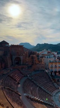 Alicante, İspanya, 9 Ağustos 2025: Cartagena 'daki Roma Tiyatrosu manzarası yükseltildi. Antik Roma tiyatrosunun yüksek açılı çekimleri şehir binaları ve dağlarla harabeler oluşturuyor.