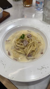 Gourmet Kremalı Spagetti Carbonara Makarnası Kara Biber ve Minimalist Beyaz Tabakta Taze Bitkiler