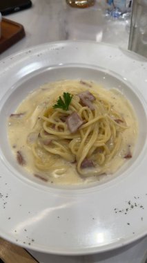 Gourmet Kremalı Spagetti Carbonara Makarnası Kara Biber ve Minimalist Beyaz Tabakta Taze Bitkiler