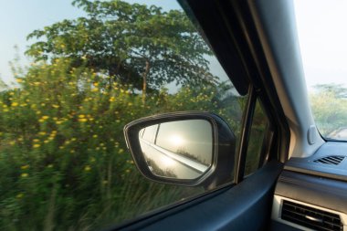 Arabanın pencere çerçevesi ve gösterge paneli ile gökyüzünü ve güneşi yansıtan bir aracın yan aynası