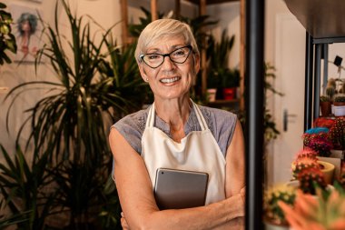 Çiçekçisinde çalışan tabletli yaşlı kadın çiçekçinin portresi..