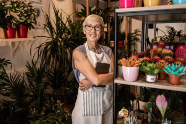 Çiçekçi dükkanında tablet kullanırken çalışan kıdemli bayan çiçekçi..