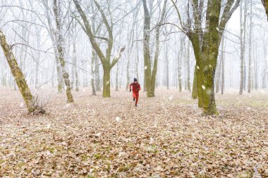 Genç adam soğuk bir kış gününde ormanda koşuyor..