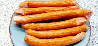 Bir tabakta yarı tütsülenmiş sosis yığını, seçici odaklanma. Yarı tütsülenmiş sosisler, ızgara veya geleneksel yemekler için ideal popüler et ürünleridir..