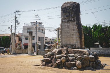 Itsukushima Tapınağı 'nda üzerinde Japon dini metni bulunan büyük taş tablet. Arka planda Matsuyama, Ehime Bölgesi, Japonya' da elektrik hatları ve binalar var.