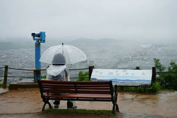 Arashiyama, Kyoto, Japonya 'da yağmurlu bir günde Iwatayama Maymun Parkı' nda şemsiye tutan yalnız bir adam tek başına oturuyor.