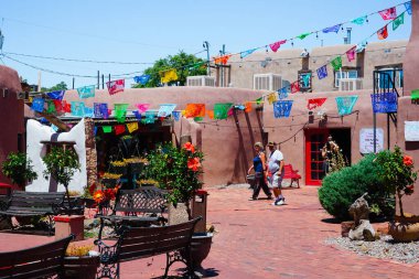 Albuquerque, New Mexico, ABD 'de güneşli bir günde Albuquerque' nin Eski Şehir Mahallesi 'ndeki kerpiç binalarıyla bir meydanda yürüyen turistler görülüyor.