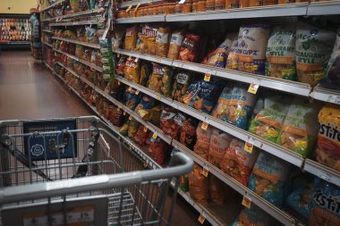 An empty shopping cart in a dark aisle with potato chips and other snacks inside a Smith's grocery store in Albuquerque, NM, USA