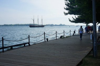 Toronto 'daki Ontario Gölü' nün kıyısındaki bir patikada yürüyen yayalar Toronto, Ontario, Kanada 'da bir turist yolcu teknesiyle Toronto Adası' na doğru yürüyorlar.