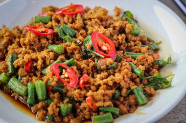 Acı biberli, yeşil fasulyeli ve tuzlu soslu sığ beyaz kasede servis edilen Tayland Basil tavuğu..