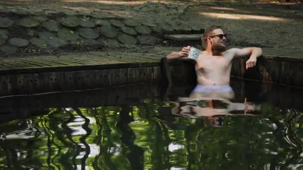是时候放松了年轻的留着胡子的男人，戴着太阳镜，光着身子坐在那里游泳 — 图库视频影像