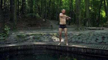 Egzersiz yapan genç adam ellerini ormanda hareket ettiriyor, esneme hareketleri yapıyor, atletizm yapıyor.