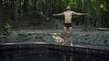 Egzersiz yapan genç adam ellerini ormanda hareket ettiriyor, esneme hareketleri yapıyor, atletizm yapıyor.