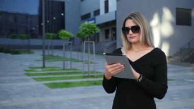 Finans bölgesinde güneş gözlüğü takan iş kadını dijital tablet kullanıyor