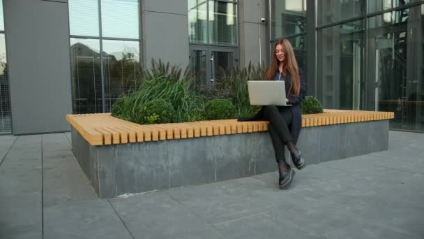 Mujer de negocios utiliza portátil contra edificio de oficinas. Mujer de negocios caucásica — Vídeo de stock